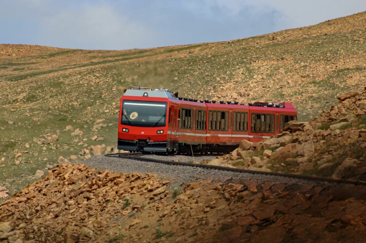 Modern red Pikes Peak Cog Railway train crossing a rocky alpine slope near the summit